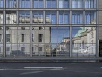 a large building is reflected in the side of the street that goes along this narrow road