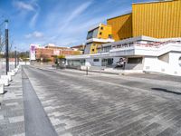 a city street that has yellow and white buildings in the back ground and a brown and white building with orange balconies at each corner