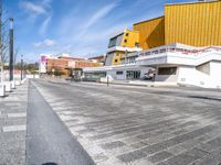 a city street that has yellow and white buildings in the back ground and a brown and white building with orange balconies at each corner