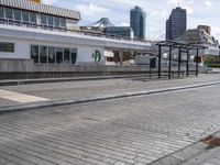 the empty brick walkway is by the water next to the train station and buildings in a city