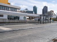 the empty brick walkway is by the water next to the train station and buildings in a city