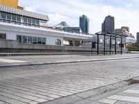 the empty brick walkway is by the water next to the train station and buildings in a city