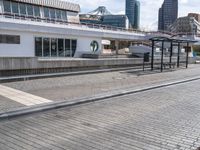 the empty brick walkway is by the water next to the train station and buildings in a city