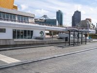 the empty brick walkway is by the water next to the train station and buildings in a city