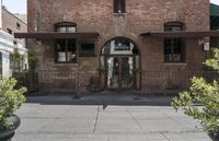 the entrance is made of brick with arched window frames and arched doors a potted plant can be seen in front