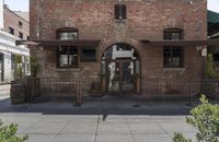 the entrance is made of brick with arched window frames and arched doors a potted plant can be seen in front