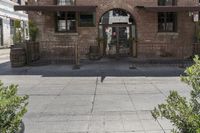 the entrance is made of brick with arched window frames and arched doors a potted plant can be seen in front