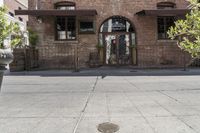 the entrance is made of brick with arched window frames and arched doors a potted plant can be seen in front