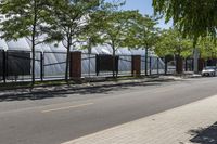 a tree - lined sidewalk is next to a row of bricked - in fences