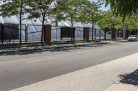 a tree - lined sidewalk is next to a row of bricked - in fences