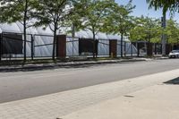 a tree - lined sidewalk is next to a row of bricked - in fences