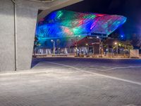 a modern building in a city at night with bright lights glowing on the facade and a bench to the left