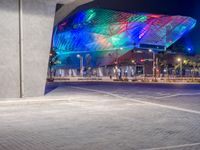 a modern building in a city at night with bright lights glowing on the facade and a bench to the left