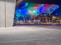 a modern building in a city at night with bright lights glowing on the facade and a bench to the left