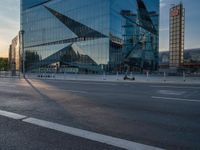 a person sits in the road alone on their motorcycle near a building that has a glass facade