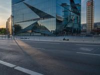 a person sits in the road alone on their motorcycle near a building that has a glass facade