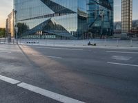 a person sits in the road alone on their motorcycle near a building that has a glass facade