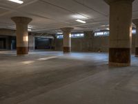 an empty concrete warehouse with multiple pillars in the center and three people walking on the floor