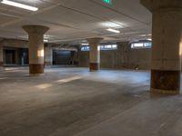 an empty concrete warehouse with multiple pillars in the center and three people walking on the floor