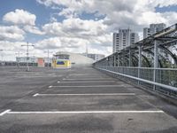 a paved parking lot with a small white building in the background of a large, gray city with a parking area in front of it