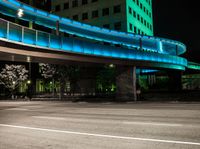 the empty road next to a big building has a lighted bridge over it on top