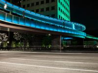 the empty road next to a big building has a lighted bridge over it on top