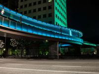 the empty road next to a big building has a lighted bridge over it on top