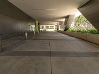 a modern concrete building has a long and wide sidewalk with grey cement floors and an arched roof