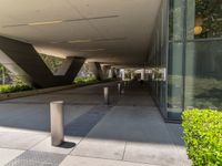 a walkway at a modern building that is made of metal poles and posts, with plants on either side