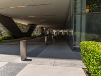 a walkway at a modern building that is made of metal poles and posts, with plants on either side