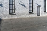 several windows near a white brick wall, next to a sidewalk with an open door