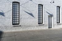 several windows near a white brick wall, next to a sidewalk with an open door