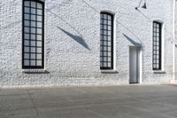 several windows near a white brick wall, next to a sidewalk with an open door