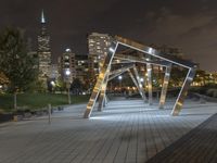 an open structure with city lights in the distance and a building on each side and two trees,