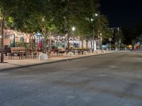 an empty street with many tables along it in the night time, and people walking on the sidewalk