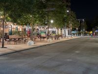 an empty street with many tables along it in the night time, and people walking on the sidewalk