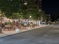 an empty street with many tables along it in the night time, and people walking on the sidewalk