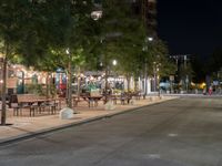 an empty street with many tables along it in the night time, and people walking on the sidewalk