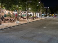 an empty street with many tables along it in the night time, and people walking on the sidewalk