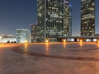 the illuminated urban city skyline is visible from a rooftop top at night time of a circular plaza