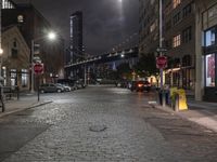 the road and street signs at night, showing a bridge in the distance with cars parked near the curb