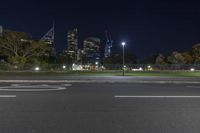 city lights are shining behind a street sign on a pavement next to a fence and grassy area