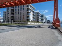 a long dock with concrete bricks beside a marina area with orange structures and buildings on the other side