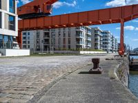 a long dock with concrete bricks beside a marina area with orange structures and buildings on the other side