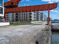 a long dock with concrete bricks beside a marina area with orange structures and buildings on the other side