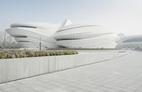 a building that is curved and white with some bushes in front of it and people on the side