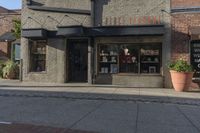 the front entrance to a small store in a city area with potted plants and small windows