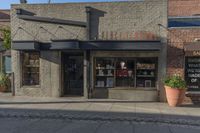 the front entrance to a small store in a city area with potted plants and small windows