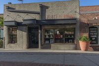 the front entrance to a small store in a city area with potted plants and small windows