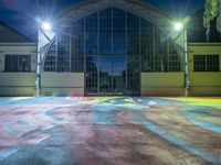 a painted playground at night with light shining down and a sports court in the background